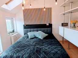 Schlafzimmer mit schwarzem Bett, Kissen und minimalistischer Dekoration.