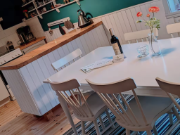 Helle Küche mit Essbereich, Tisch, Stühlen, Weinflasche und Blumentopf.