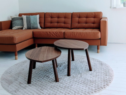 Brauner Sofa mit Kissen, zwei Tischchen und Teppich in hellem Raum.