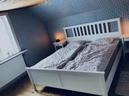 Helles Schlafzimmer mit einem weißen Bett und Nachttisch, dekoriert mit Tapete.